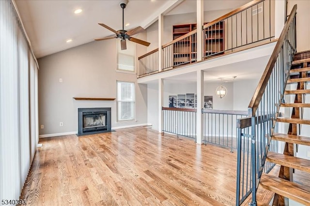 unfurnished living room with baseboards, a ceiling fan, a fireplace with flush hearth, wood finished floors, and high vaulted ceiling