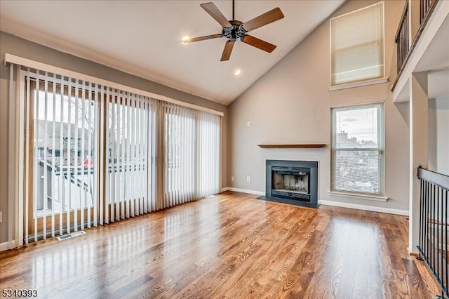 unfurnished living room featuring a healthy amount of sunlight, a fireplace with flush hearth, baseboards, and wood finished floors