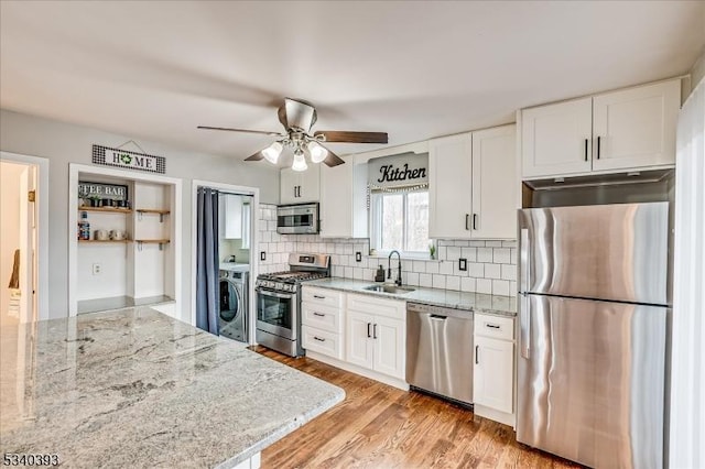 kitchen featuring light wood finished floors, decorative backsplash, appliances with stainless steel finishes, washer / clothes dryer, and white cabinetry