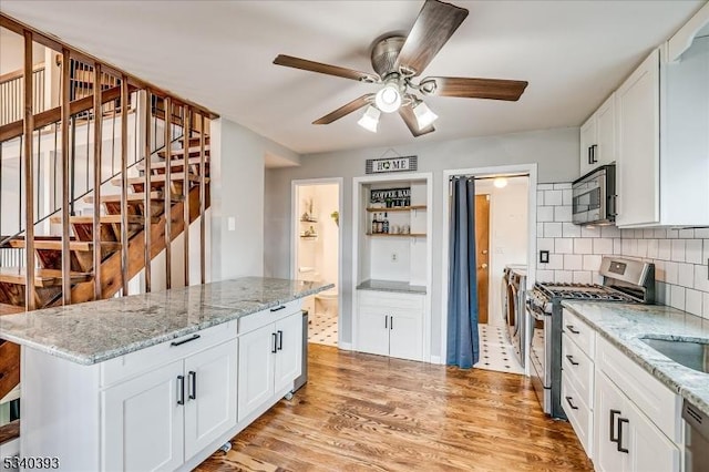 kitchen with light wood finished floors, tasteful backsplash, appliances with stainless steel finishes, white cabinetry, and independent washer and dryer