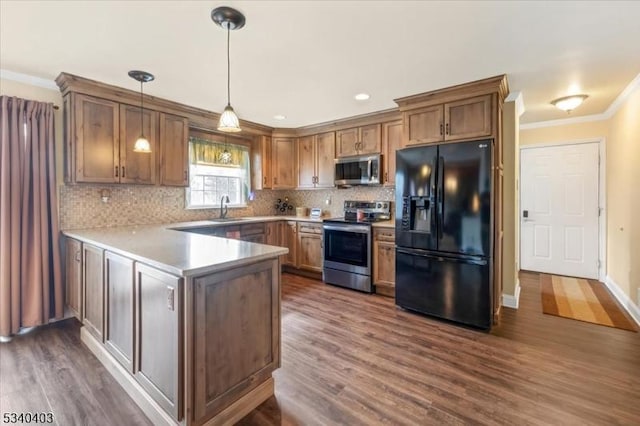 kitchen featuring ornamental molding, dark wood-type flooring, a peninsula, stainless steel appliances, and a sink