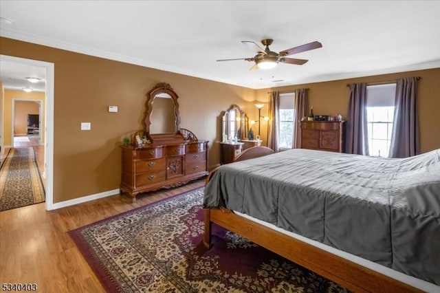 bedroom with crown molding, wood finished floors, a ceiling fan, and baseboards