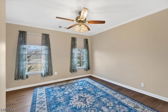 empty room with ornamental molding, wood finished floors, visible vents, and baseboards