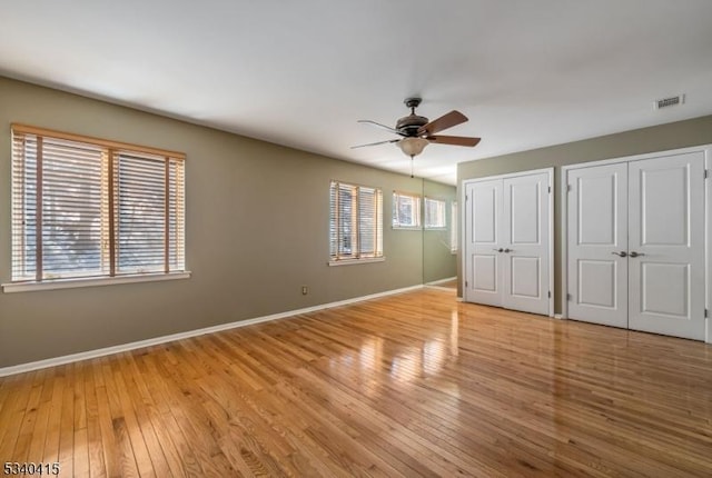 unfurnished bedroom featuring ceiling fan, visible vents, baseboards, multiple closets, and wood-type flooring