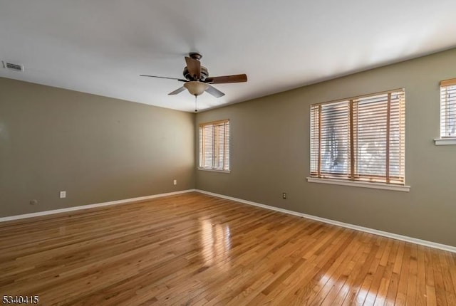 unfurnished room featuring light wood finished floors, a healthy amount of sunlight, visible vents, and baseboards