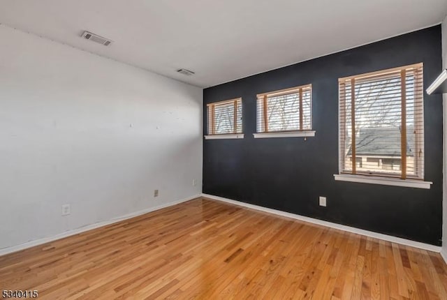 spare room with light wood-type flooring, visible vents, and baseboards