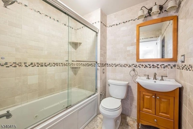 full bath featuring toilet, shower / bath combination with glass door, vanity, and tile walls