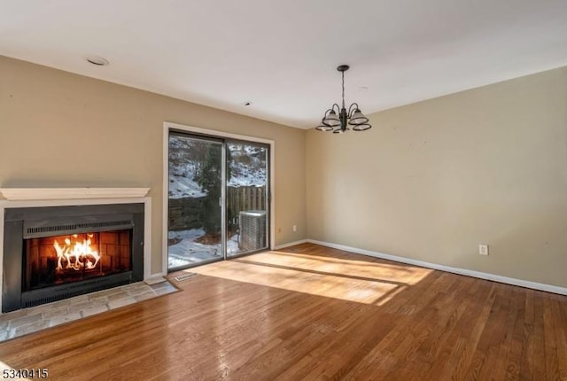 unfurnished living room with a fireplace with flush hearth, a chandelier, wood finished floors, and baseboards