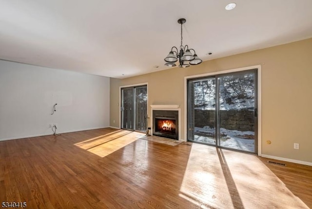 unfurnished living room with baseboards, visible vents, a fireplace with flush hearth, wood finished floors, and a chandelier