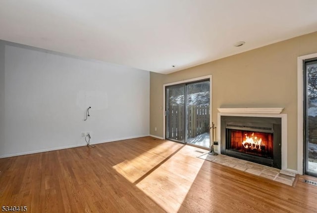 unfurnished living room with a fireplace with flush hearth, wood finished floors, and baseboards