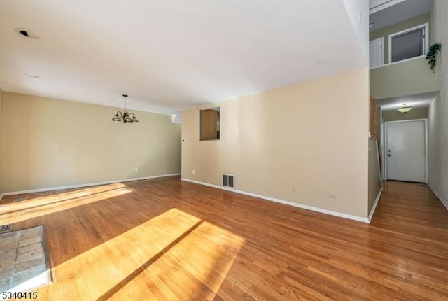 unfurnished room with baseboards, a notable chandelier, visible vents, and wood finished floors