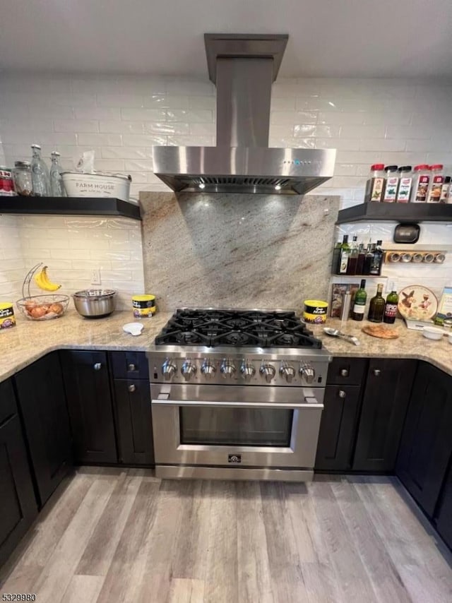 kitchen featuring wall chimney exhaust hood, high end stove, light wood-style flooring, and light stone countertops