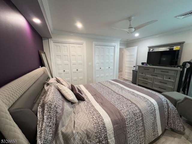 bedroom with ornamental molding, visible vents, ceiling fan, and two closets