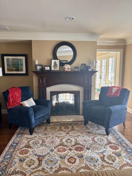 sitting room with ornamental molding, a multi sided fireplace, and wood finished floors