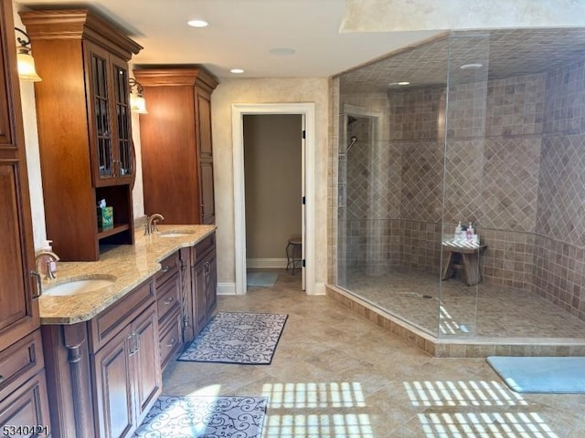 bathroom with double vanity, walk in shower, a sink, and baseboards