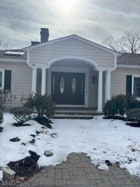 snow covered property entrance featuring a chimney