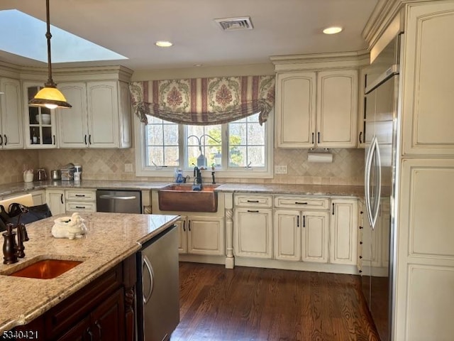 kitchen featuring visible vents, appliances with stainless steel finishes, hanging light fixtures, light stone countertops, and a sink