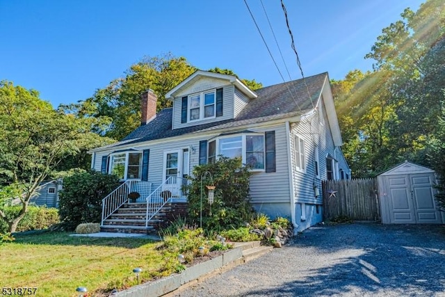 bungalow featuring an outbuilding, a storage shed, fence, a chimney, and a front yard