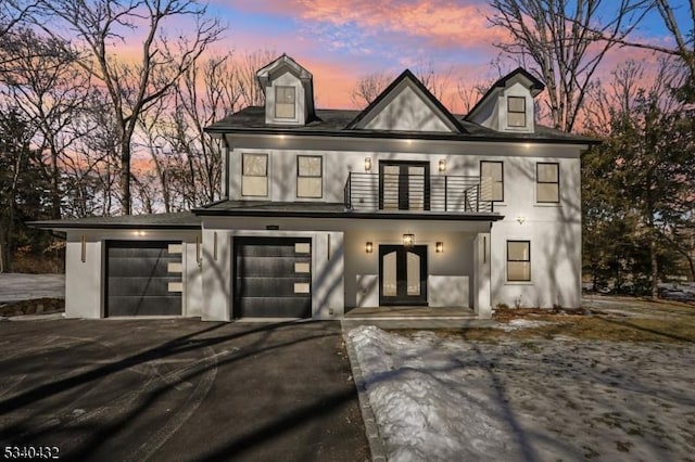 view of front of house with aphalt driveway, a balcony, a garage, french doors, and stucco siding