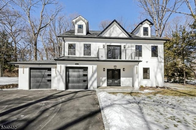 view of front of house with aphalt driveway, a balcony, a garage, french doors, and stucco siding