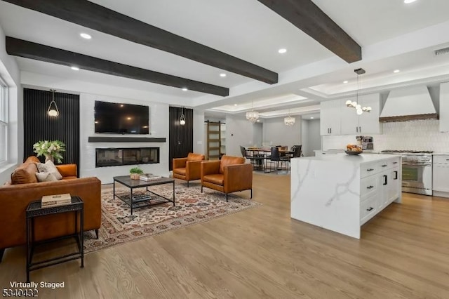 living room featuring visible vents, beamed ceiling, light wood-type flooring, a fireplace, and a chandelier