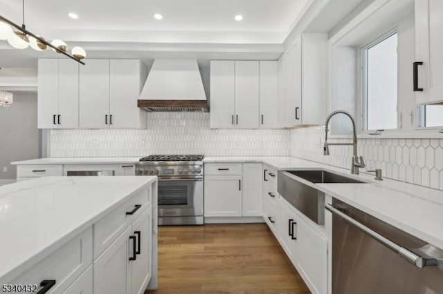 kitchen featuring stainless steel appliances, white cabinets, premium range hood, and a sink