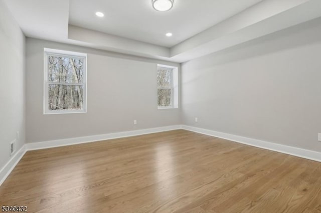 unfurnished room with a tray ceiling, recessed lighting, wood finished floors, and baseboards