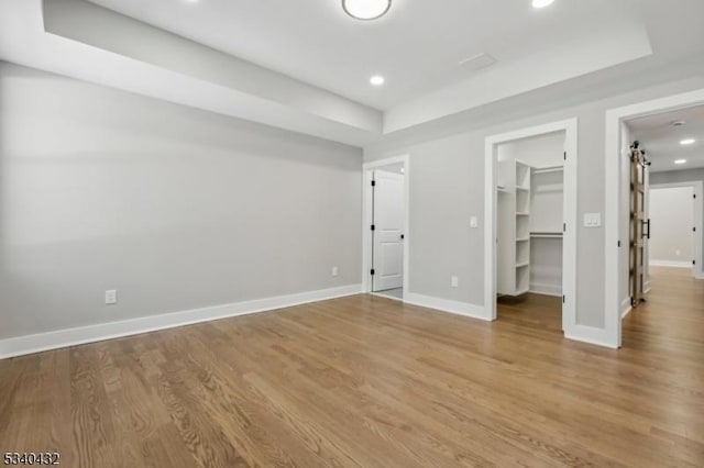 unfurnished bedroom with a raised ceiling, recessed lighting, wood finished floors, and baseboards