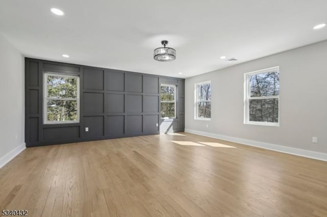 spare room featuring light wood-style flooring, baseboards, a decorative wall, and recessed lighting