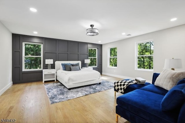 bedroom featuring light wood finished floors, baseboards, a decorative wall, and recessed lighting