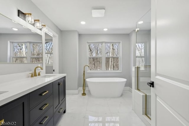 full bath featuring a freestanding tub, plenty of natural light, marble finish floor, and a sink