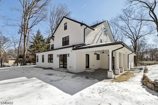 snow covered rear of property with entry steps, ceiling fan, and stucco siding