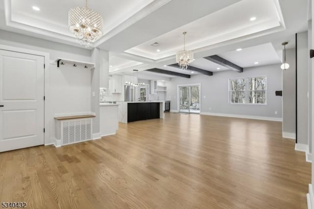 unfurnished living room with light wood-style floors, a tray ceiling, a notable chandelier, and baseboards