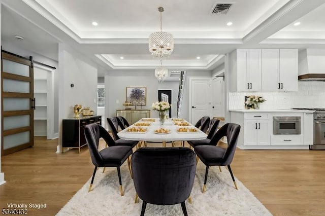 dining area featuring an inviting chandelier, a barn door, a tray ceiling, and light wood-style floors