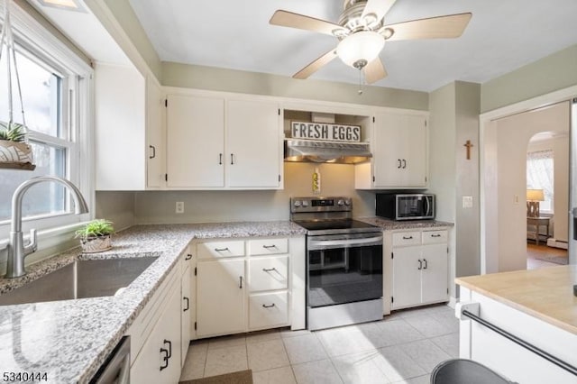 kitchen with arched walkways, light tile patterned floors, under cabinet range hood, stainless steel appliances, and a sink