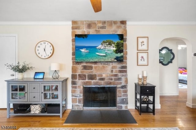 living area featuring a fireplace, arched walkways, crown molding, and wood finished floors