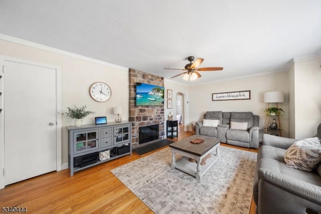 living room featuring a brick fireplace, a ceiling fan, ornamental molding, and wood finished floors