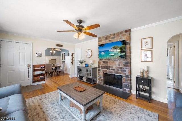 living room with arched walkways, ceiling fan, ornamental molding, wood finished floors, and a fireplace