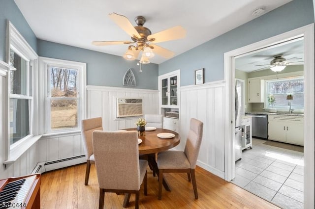 dining area featuring an AC wall unit, wainscoting, light wood finished floors, and baseboard heating