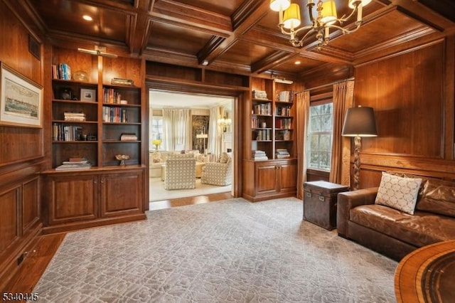 sitting room featuring an inviting chandelier, wooden walls, built in shelves, and coffered ceiling