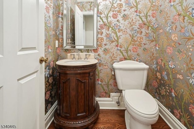 bathroom featuring wallpapered walls, baseboards, toilet, wood finished floors, and vanity