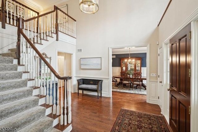 entrance foyer featuring dark wood-style floors, visible vents, ornamental molding, a decorative wall, and a notable chandelier