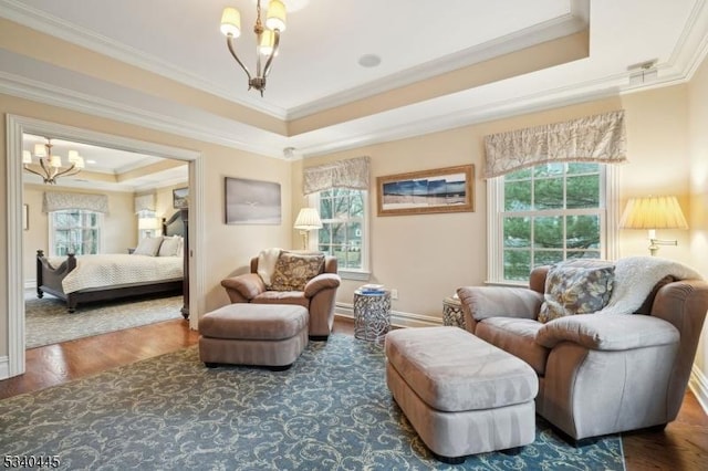 living area with a chandelier, a healthy amount of sunlight, a tray ceiling, and wood finished floors