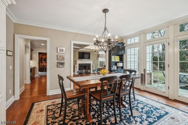 dining room featuring a notable chandelier, wood finished floors, a fireplace, crown molding, and baseboards