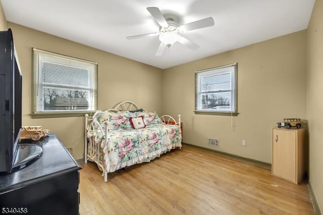 bedroom with a ceiling fan, light wood-type flooring, visible vents, and baseboards