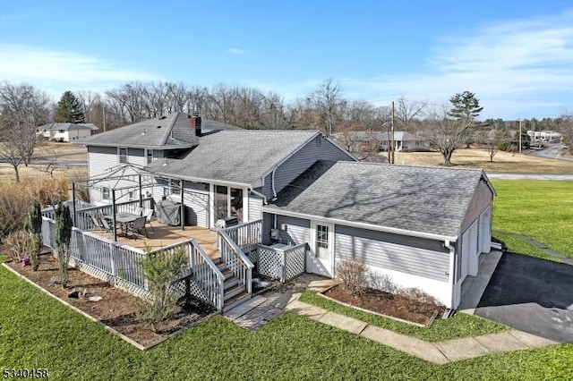 view of front facade featuring aphalt driveway, roof with shingles, a wooden deck, and a front lawn