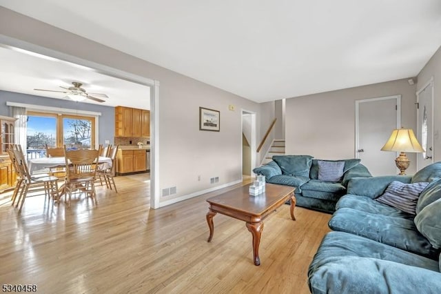 living room with light wood-type flooring, baseboards, stairs, and visible vents