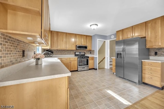 kitchen with light countertops, appliances with stainless steel finishes, a sink, and decorative backsplash