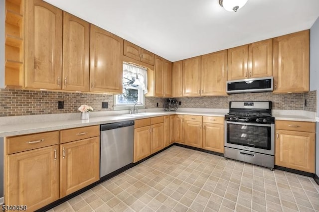 kitchen featuring appliances with stainless steel finishes, light countertops, a sink, and tasteful backsplash