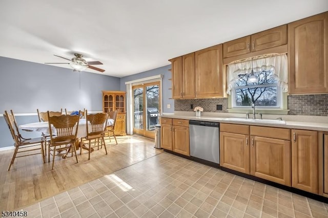 kitchen with light countertops, stainless steel dishwasher, a sink, and decorative backsplash